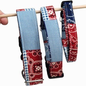 Op de afbeelding: Drie hondenhalsbanden met een patchwork-ontwerp. De halsbanden hebben een combinatie van blauw ruitjespatroon en rode paisley-patronen. Elke halsband heeft een metalen gesp en een D-ring voor het bevestigen van de lijn. De halsbanden hangen aan een houten deuvel.