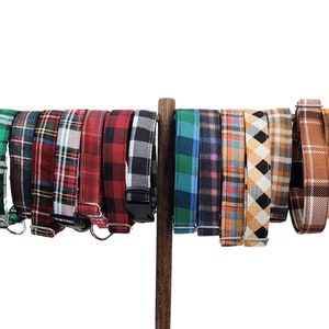 Peut inclure: Une collection de colliers pour chiens avec différents motifs écossais, dont vert, rouge, noir et orange. Chaque collier est présenté sur une tige en bois sur fond blanc. Les colliers ont des boucles métalliques.