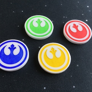 Op de afbeelding: Vier ronde witte tokens met een wit Rebel Alliance-symbool in het midden. De tokens zijn groen, rood, blauw en geel gekleurd.