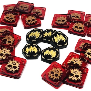 Peut inclure: Un ensemble de pions de jeu rouges et noirs avec des accents dorés. Les pions rouges sont carrés et présentent un crâne avec un œil au front. Les pions noirs sont hexagonaux et présentent une chaîne de montagnes avec un pic dentelé.