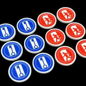 Op de afbeelding: Twaalf ronde spelstukken, zes zijn rood met een wit silhouet van een persoon die door een deur loopt, en zes zijn blauw met een wit silhouet van een sleutel.