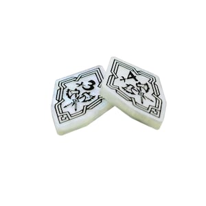 May include: Two white, diamond-shaped game pieces with black markings. One piece has a symbol and the number "x3" and the other piece has a symbol and the number "x4".