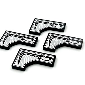 Puede incluir: Cuatro fichas de juego en blanco y negro con un diseño estilizado de hoz y cuchillo. Las fichas tienen forma rectangular con un borde curvo y un fondo texturizado. Los objetos están dispuestos sobre un fondo blanco.