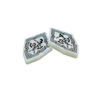 May include: Two white, diamond-shaped game pieces with black borders and intricate designs. The pieces are numbered "3" and "4" and feature a stylised image of a dragonfly.