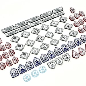 Puede incluir: Una colección de fichas de juego en varios colores y formas, incluyendo rojo, azul, blanco y negro. Las fichas presentan texto como "Combate Resuelto", "Tiro Resuelto", "Avanzar", "Mover 1", "Guardar", "Choque", "Herida", y los números 1, 2, 5 y 10.