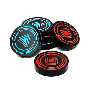 Puede incluir: Un conjunto de seis fichas de juego negras y rojas con diseños geométricos. Las fichas presentan un triángulo azul y un cuadrado rojo.