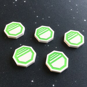 Op de afbeelding: Vijf witte achthoekige tokens met een groene rand en een wit streepontwerp in het midden.