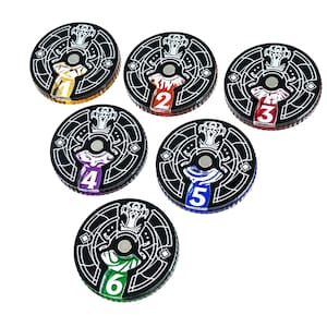 May include: A collection of six black and white game tokens. Each token has a unique colored center with a number from one to six. The tokens have a decorative design around the edges.