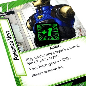 May include: A green and black card with the text "ARMORED VEST" and "UPGRADE" on it. The card has a green and black +1 symbol on it. The text on the card reads "ARMOR. Play under any player's control. Max 1 per player. Your hero gets +1 DEF. Life-saving and stylish."