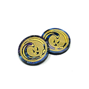 May include: Two round, blue and purple, galaxy-themed, resin dice with gold accents. The dice feature a stylized wave design with three dots in the center.