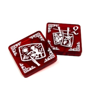 May include: Two red dice with white illustrations. One die shows a creature with a moon in the background. The other die shows two pictures hanging on a clothesline. The number 2 is printed on the die.