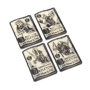 Könnte beinhalten: Vier rechteckige Spielkarten mit schwarz-weißen Illustrationen von Skeletten. Jede Karte zeigt ein anderes Skelettdesign, die Zahl 1 und den Text "KELETON Can't Move To Def."