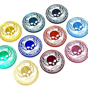 Könnte beinhalten: Zehn runde, Acryl-Token mit einem Totenkopf- und Lorbeerkranz-Design. Jeder Token hat eine andere Farbe: Rot, Blau, Grün, Gold, Silber, Schwarz, Weiß, Lila, Türkis und Pink. Der Text auf jedem Token lautet "Fear Wins Faith".