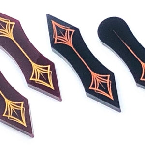 Puede incluir: Cuatro piezas decorativas en forma de flecha de acrílico con diseños dorados y naranjas. Las piezas son de diferentes colores: negro, burdeos y burdeos claro.
