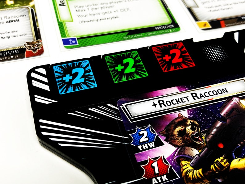May include: A black and white game board with three counters showing +2. The counters are blue, green, and red. A card with the text "Rocket Raccoon" and a picture of Rocket Raccoon is in the background.