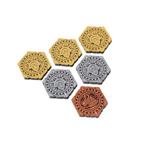 Puede incluir: Seis fichas hexagonales de juego con diseños intrincados. Las fichas son de tres colores diferentes: oro, plata y cobre. Cada ficha presenta una cabeza de animal estilizada en el centro.