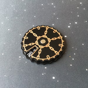 May include: Black and gold tabletop game spinner with a chain design and a number 20 printed on the side.