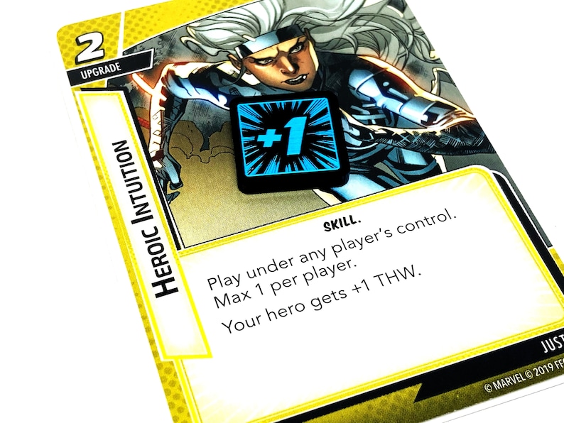 May include: A yellow card with a comic book character image and the text "HEROIC INTUITION" and "SKILL." The card has a blue and black +1 token on it. The text on the card reads "Play under any player's control. Max 1 per player. Your hero gets +1 THW."