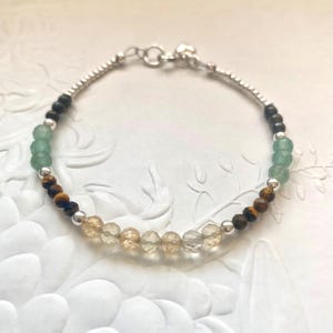Könnte beinhalten: Ein Armband mit einer Mischung aus Edelsteinen. Das Armband enthält grüne, braune und klare Perlen sowie kleine silberne Perlen. Das Armband ist an einer silbernen Kette befestigt und hat einen Verschluss.