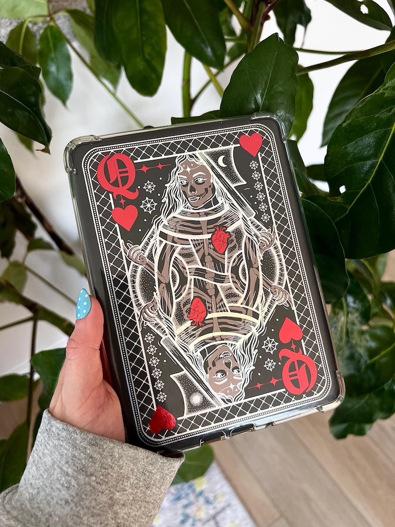 May include: Black phone case with a Queen of Hearts playing card design. The card illustration features a skeleton figure with a red heart, surrounded by red hearts and card suit symbols. The case has a clear, protective border.