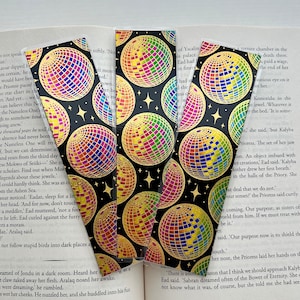 May include: Five gold and rainbow disco ball bookmarks with a black background. The bookmarks are made of clear plastic with a gold foil design.