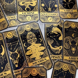May include: A set of twelve gold foil zodiac tarot cards with black backgrounds. Each card features a zodiac symbol, constellation, and astrological illustration.