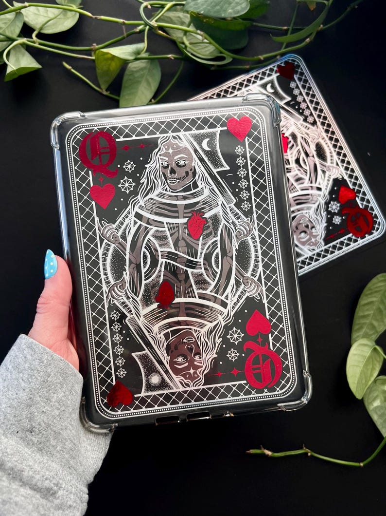May include: Clear phone case with a Queen of Hearts playing card design. The case has a black background with a skeletal figure holding a sword, red hearts, and decorative elements. Another case is visible in the background.