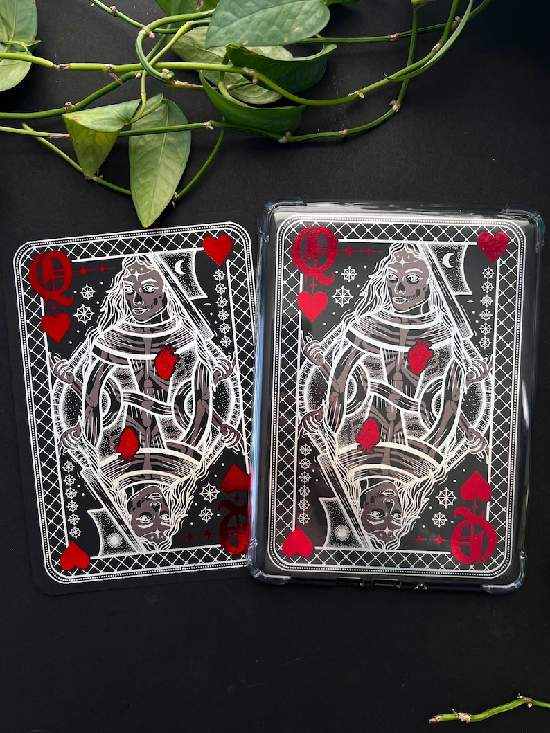 May include: Two playing cards featuring a Queen of Hearts design with a skeletal figure, red hearts, and intricate white detailing on a black background. One card is in a clear protective case.