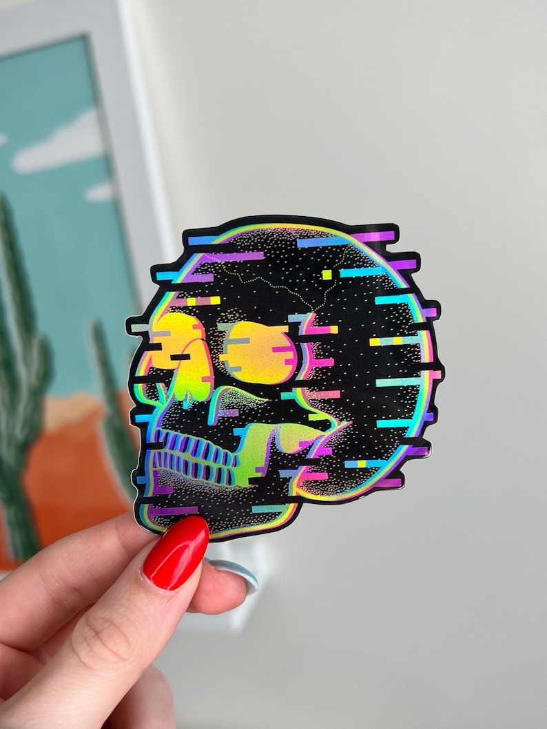 May include: A holographic sticker of a skull with a glittery, pixelated design. The skull is outlined in rainbow colors and has a black background.
