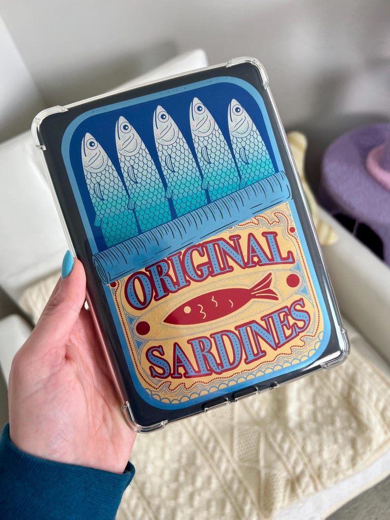 May include: A clear phone case with a design of a blue and yellow sardine can. The can has the text "ORIGINAL SARDINES" and a red fish illustration.