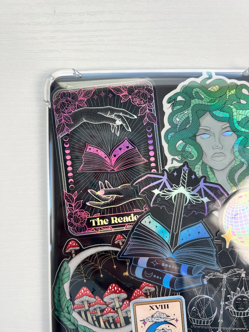 May include: A collection of holographic stickers featuring a tarot card with the text "The Reader", a sword in a book, a mushroom patch, a crescent moon, and a Medusa with green hair.