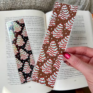 May include: Two Christmas-themed bookmarks with a repeating pattern of stylized Christmas trees. The trees are decorated with red and white stripes and green leaves. One bookmark has a brown background and the other has a black background.