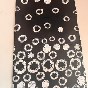 May include: Black fabric featuring a repeating pattern of white circles with a textured appearance. Some circles have a blue, marbled effect. Suitable for clothing or home decor.