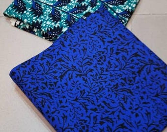 May include: Two folded fabric pieces. One is teal with a white and navy leaf pattern. The other is royal blue with a black floral design. The fabrics are likely for sewing, quilting, or crafting projects.