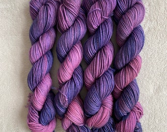 May include: Four skeins of yarn in shades of purple and pink. The yarn is a gradient colour, with the purple shades fading into the pink shades.