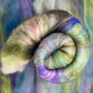 Puede incluir: Primer plano de una madeja de hilo teñido a mano en tonos de verde, azul, morado y blanco. El hilo está enrollado en forma de espiral.