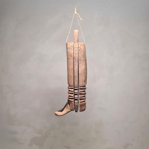 Puede incluir: Un objeto de madera con forma de bota que cuelga de una cuerda. La bota está hecha de varias piezas de madera que están unidas. La bota es de color marrón claro.