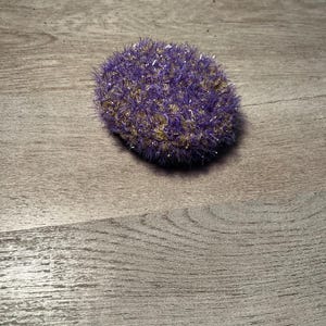 May include: A purple and gold scrubby sponge with a textured surface.