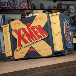 May include: A custom computer case featuring the X-Men logo. The case is primarily black with gold and red accents. The X-Men logo is prominently displayed on the front. The case has a unique, geometric design.