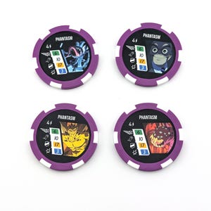 May include: Four circular game tokens with purple and white edges. Each token features a different monster illustration and the word "PHANTASM". The tokens also display various numerical values and symbols.