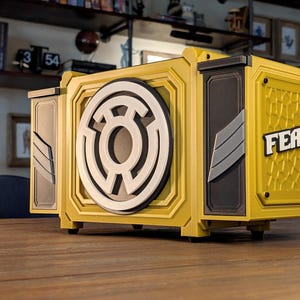 May include: Yellow and black box with a white and black circular design on the front. The word "FEAR" is displayed in white on the side. The box is sitting on a wooden surface.