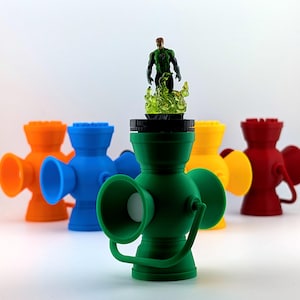 May include: A collection of colorful, 3D-printed lanterns in orange, blue, yellow, and red, with a green lantern in the foreground. A Green Lantern action figure stands atop the green lantern, surrounded by a green flame effect.