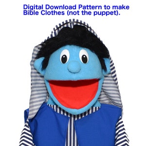 May include: A blue puppet with black hair, wearing a blue and white striped shirt and a blue vest. The puppet has a large, open mouth and is smiling.