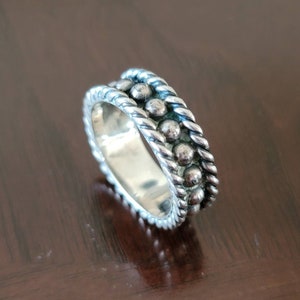 May include: A silver ring with a beaded and rope design. The ring is wide and has a polished finish.