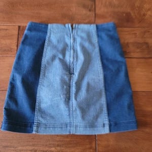 Puede incluir: Minifalda vaquera con dise&ntilde;o de bloques de color. La falda presenta un panel central azul claro flanqueado por paneles laterales azul oscuro. Una cremallera recorre la espalda. La falda est&aacute; hecha de un material vaquero resistente.