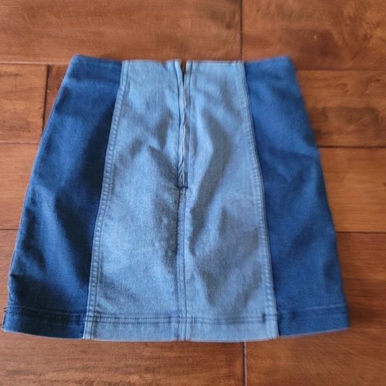 Puede incluir: Minifalda vaquera con dise&ntilde;o de bloques de color. La falda presenta un panel central azul claro flanqueado por paneles laterales azul oscuro. Una cremallera recorre la espalda. La falda est&aacute; hecha de un material vaquero resistente.