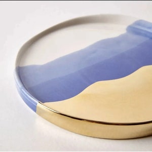 Puede incluir: Un plato redondo de cer&aacute;mica con un borde dorado. El plato est&aacute; decorado con un dise&ntilde;o abstracto azul y amarillo.