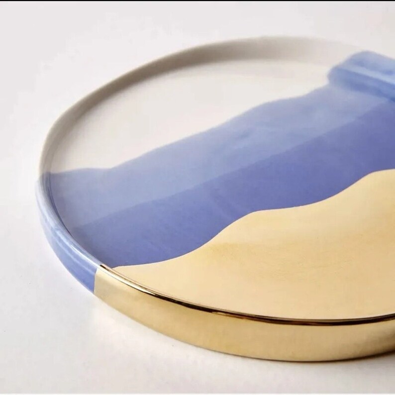 Puede incluir: Un plato redondo de cer&aacute;mica con un borde dorado. El plato est&aacute; decorado con un dise&ntilde;o abstracto azul y amarillo.
