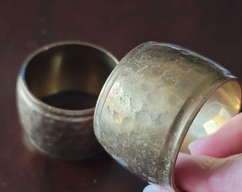 Può includere: Due anelli per tovaglioli in ottone con finitura martellata. Gli anelli sono rotondi e hanno un aspetto leggermente usurato.