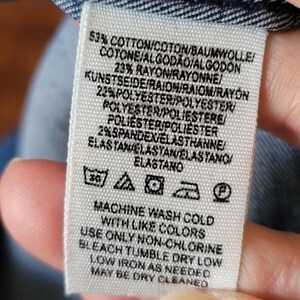 Puede incluir: Primer plano de una etiqueta de tela blanca con texto negro. La etiqueta detalla la composici&oacute;n de la tela: 53% algod&oacute;n, 23% ray&oacute;n, 22% poli&eacute;ster y 2% elastano. Tambi&eacute;n se imprimen instrucciones de lavado.